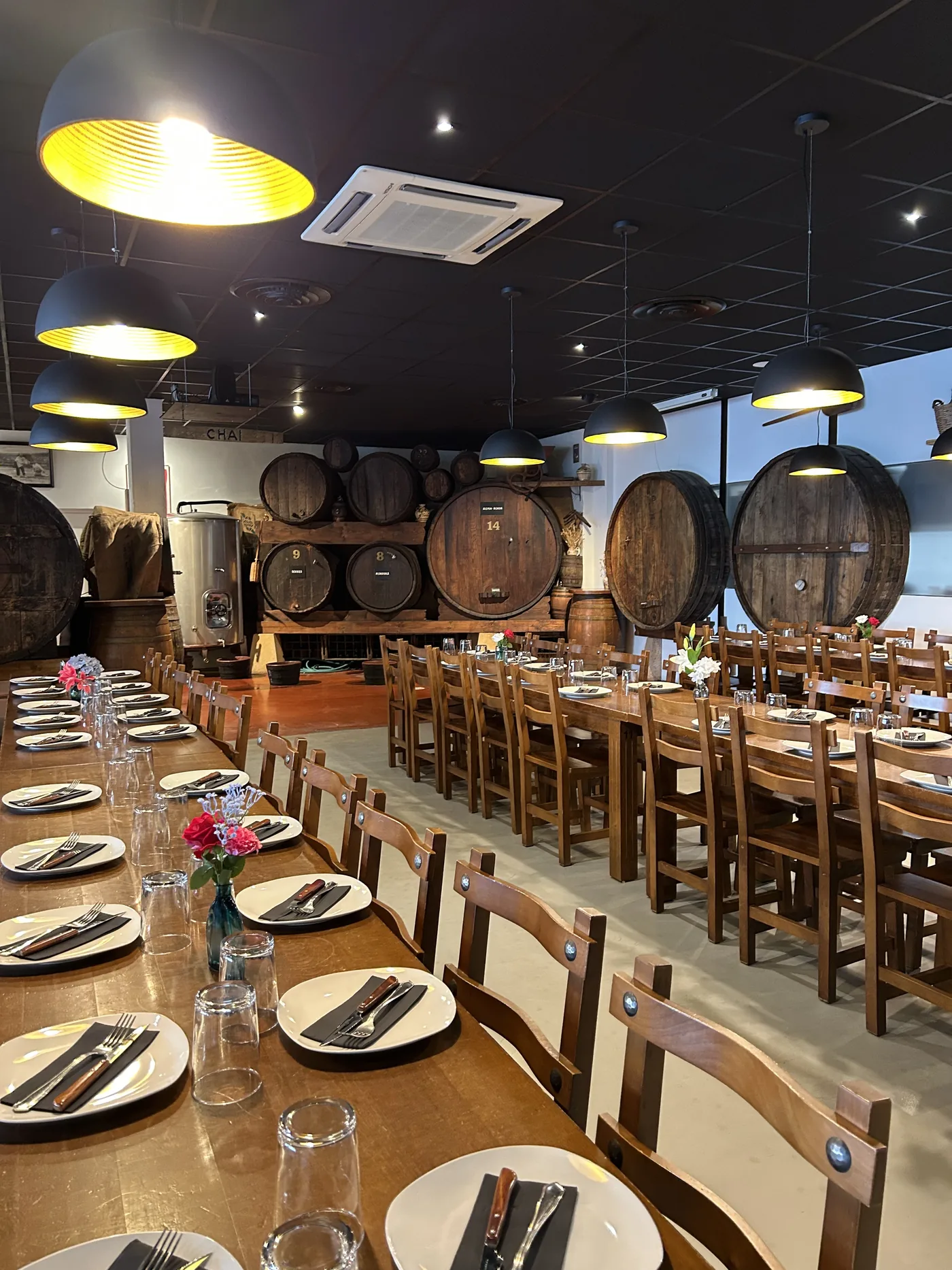 La grande salle de la Cidrerie Berri dressée pour le service, devant les fûts de chêne du chai et la cuve de fermentation